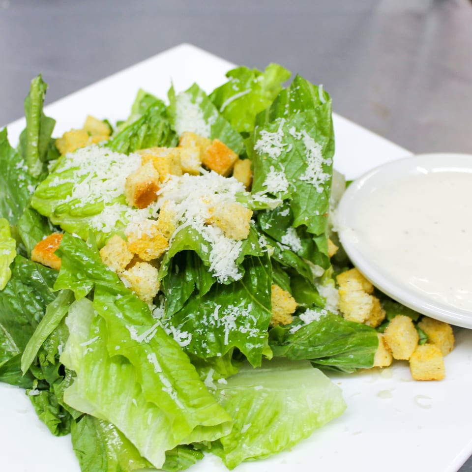 Caesar salad with romaine lettuce, croutons, grated Parmesan, and creamy dressing served on a white plate.