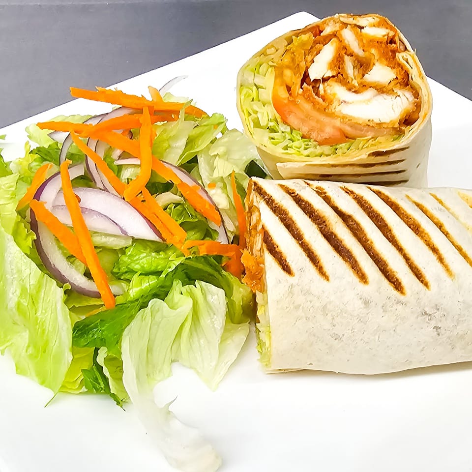 Grilled chicken wrap with lettuce, tomato, and carrots served alongside a fresh salad on a white plate.