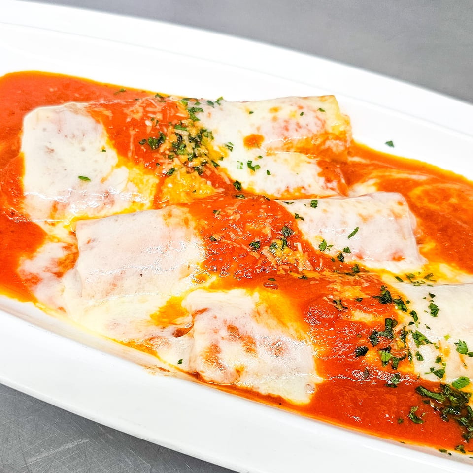 Cheese-filled pasta rolls covered in tomato sauce, melted cheese, and chopped herbs on a white rectangular plate.