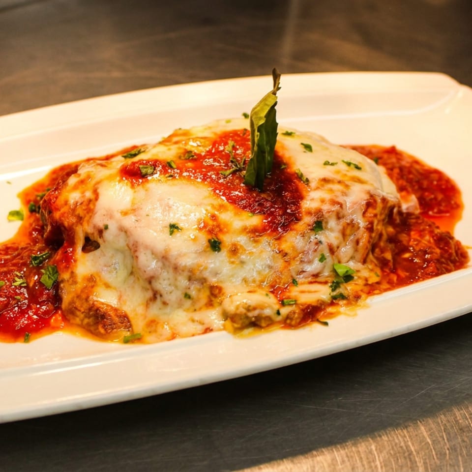 A rectangular white plate holds a serving of lasagna topped with melted cheese, marinara sauce, and basil.