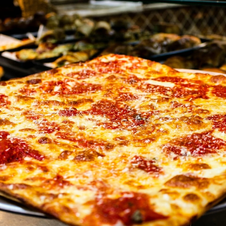 A large, rectangular cheese pizza with bright red sauce and melted mozzarella, on a metal tray.