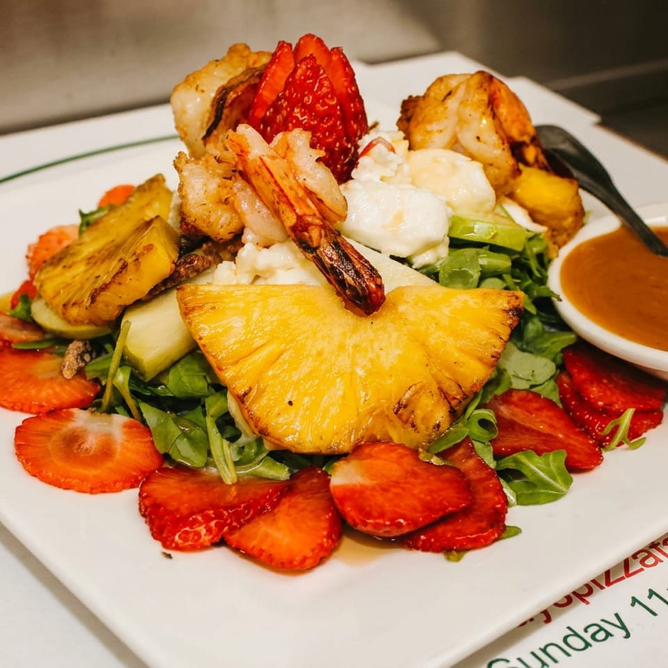 A vibrant salad with grilled shrimp, pineapple, strawberries, and mozzarella, served with a side of dressing.